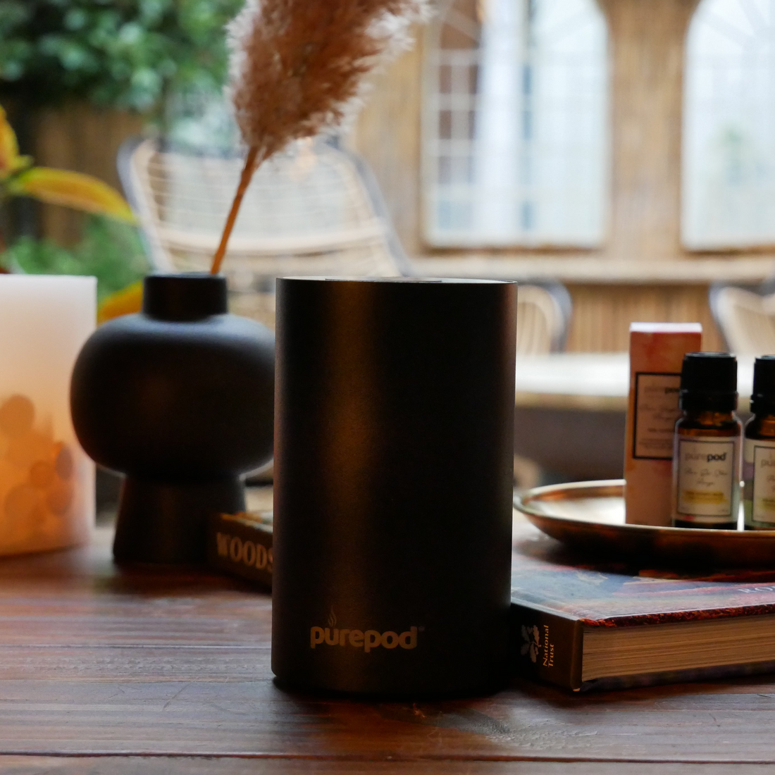 Black PurePod home diffuser on a wooden table with a candle and book