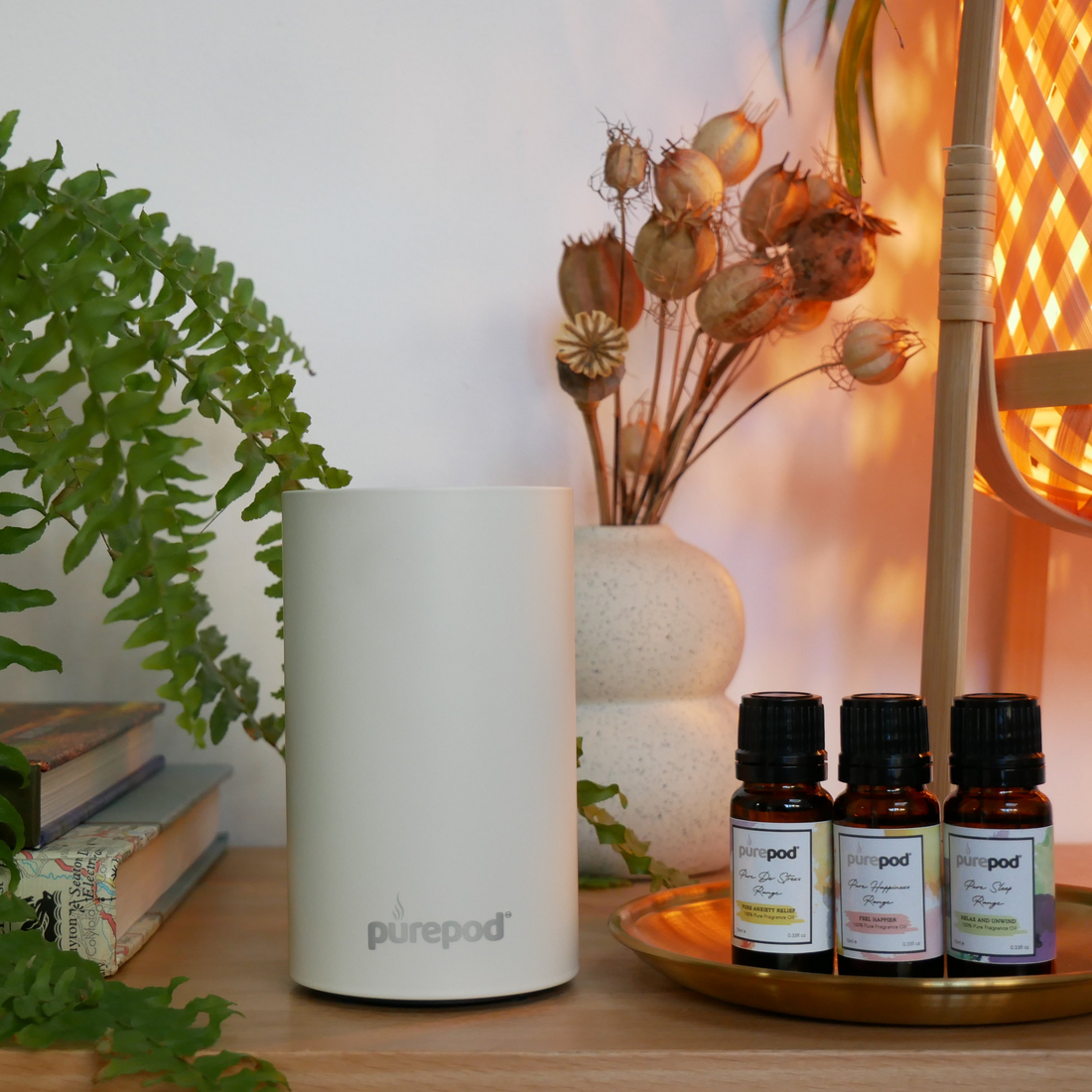 PurePod home diffuser with three fragrance oils on a brass tray beside a plant and books